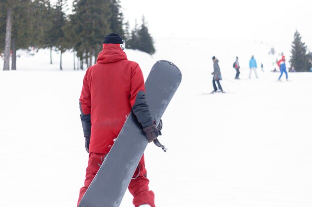 Zdjęcie koncepcja zimy, wypoczynku, sportu i ludzi - snowboardzista w kasku stojący na samym szczycie góry i trzymający snowboard za plecami