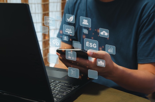 Koncepcja zrównoważonego biznesu (środowiskowe, społeczne, zarządzanie: ESG). Ręka trzyma telefon ikona biznes wirtualny na tle ekranu.