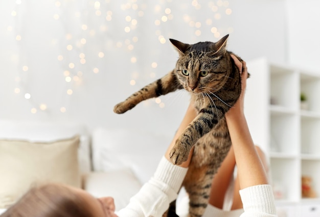 koncepcja zwierząt domowych, komfortu, świąt Bożego Narodzenia, zimy i ludzi - młoda kobieta z kotem leżącym w łóżku w domu