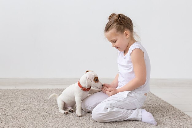 Koncepcja zwierząt, dzieci i zwierząt domowych - małe dziecko dziewczynka siedzi na podłodze z cute puppy i gry.