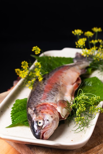 Koncepcja żywności Biały pstrąg rybny w ceramicznym talerzu na drewnianej desce na czarnym tle z miejscem na kopię