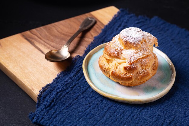 Koncepcja żywności Domowe świeże pieczone Choux a la creme, krem Ptyś, krem Choux w białej płycie ceramicznej na czarnym tle z miejscem na kopię