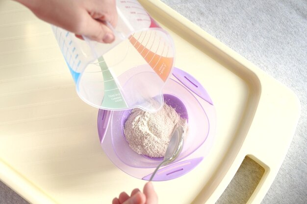 koncepcja żywności i odżywiania niemowląt ręce matki z słoikiem łyżką i miską przygotowujące płatki z proszku z bliska