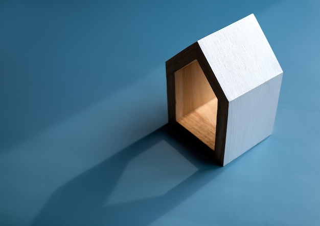 Koncepcje inwestycji w dom rodzinny w nieruchomości Biały minimalny miniaturowy drewniany mały dom na białym tle na ciemnoniebieskim tle ze światłem i cieniem z miejsca kopiowania