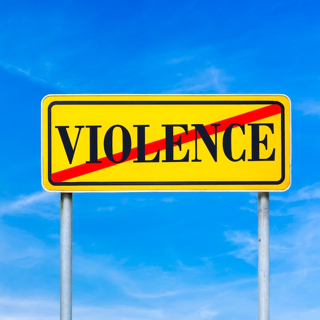 Koncepcyjne obraz jasnożółty znak drogowy przedstawiający Przemoc zabroniona słowem - Przemoc - przekreślona na tle błękitnego nieba.