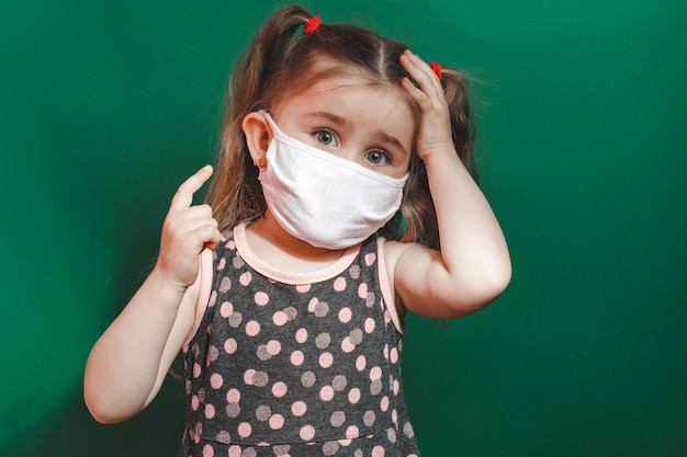 Koncepcyjne Zdjęcie Dziewczynki W Masce Medycznej Pokazuje Palec Wskazujący Na Zielonym Tle Z Bliska 2020