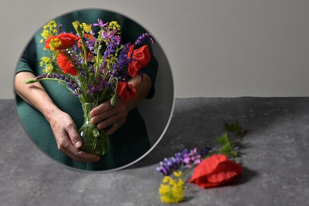 Zdjęcie konceptualna kobieta trzymająca różne kwiaty w wazonie i lustro