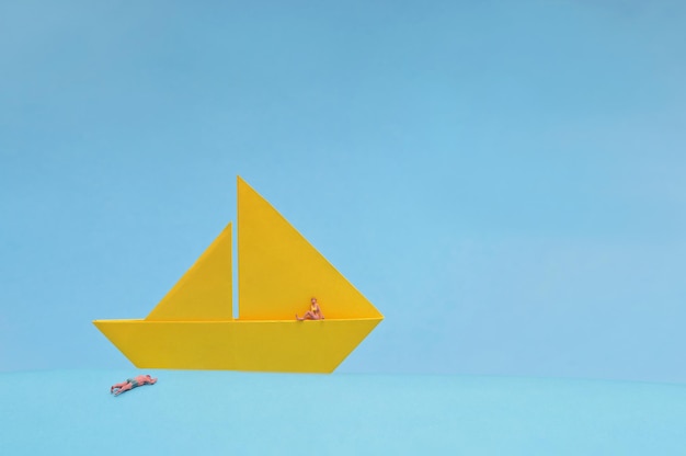 Zdjęcie konceptualna żółta papierowa łódź i miniaturowi ludzie na niebieskim tle