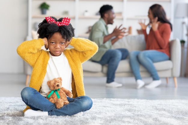 Konflikty rodzinne denerwują czarną dziewczynę zamykającą uszy rękami podczas kłótni rodziców