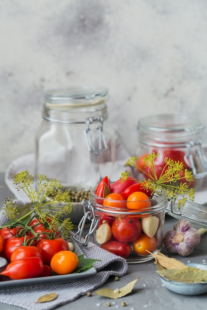 Konserwowanie świeżych i marynowanych pomidorów, przypraw i czosnku na szarym stole.