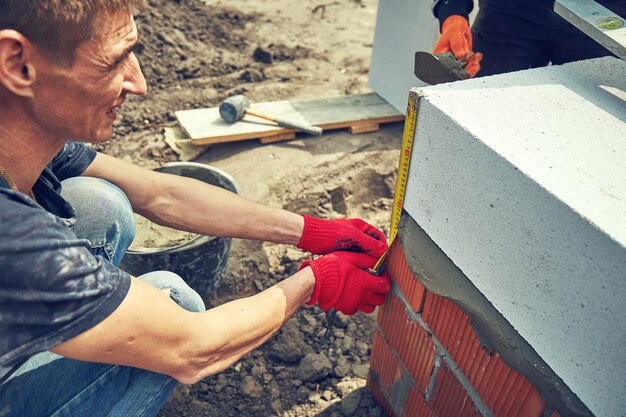 Zdjęcie konstruktor kładzie blok z betonu komórkowego na placu budowy