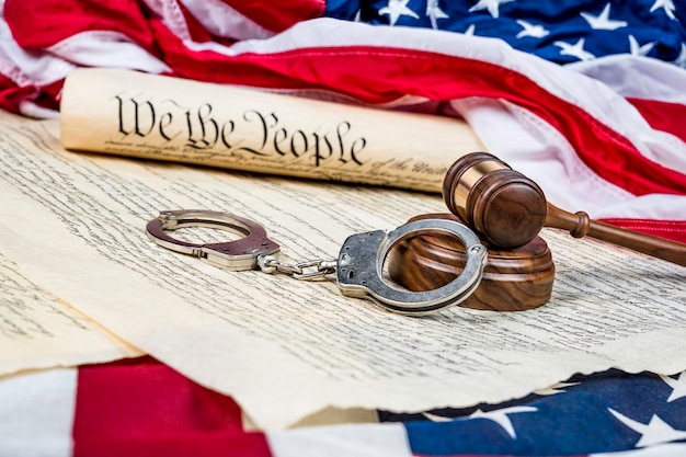 Zdjęcie konstytucja stanów zjednoczonych zwinięta na amerykańskiej fladze z młotkiem i kajdankami na pierwszym planie