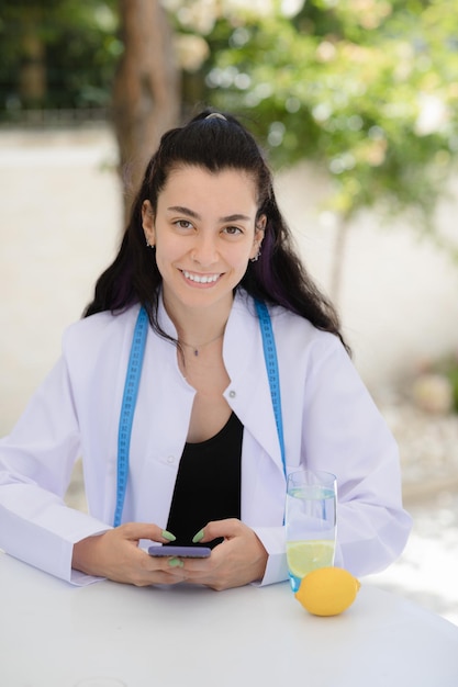 Zdjęcie konsultacja detoks online lekarz dietetyk siedzi przy stole i trzyma telefon komórkowy w dłoniach, uśmiechając się i patrząc do kamery