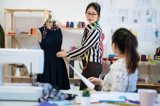 Konsultanci Project managera młodego projektanta. Dwie azjatyckie Japonki w studiu projektowym pracujące na manekinie wraz z nową sukienką. pracownica rozmawia krawiec z modelem manekina w warsztacie.