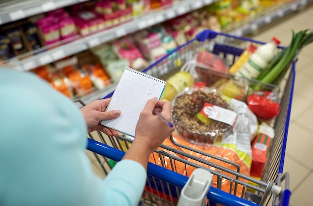 konsumpcjonizm i koncepcja ludzi - kobieta z notebookem i wózkiem zakupowym lub wózkiem kupującym żywność w sklepie spożywczym lub supermarkecie