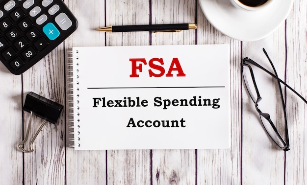 Konto FSA Flexible Spending Account jest zapisane w białym notatniku obok kalkulatora, kawy, okularów i długopisu