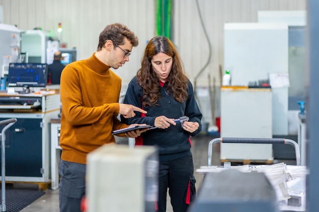 Kontrola jakości dwóch inżynierów stojących i rozmawiających podczas korzystania z tabletu w fabryce CNC