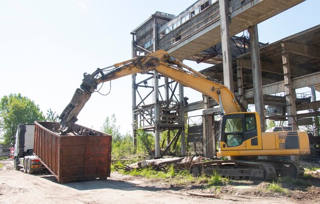 Koparka z nożycami hydraulicznymi wyburzająca stary budynek zrzucająca śmieci do kontenera