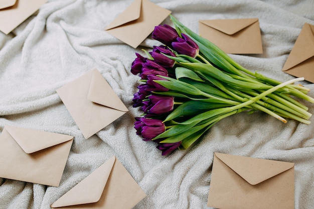 Koperty ręcznego papieru na beżowej kratce, wiosenne kwiaty, bukiet fioletowych tulipanów z kopertami.