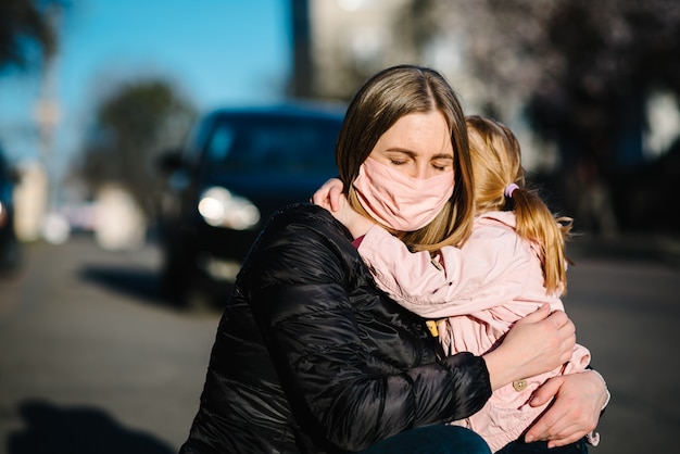 Koronawirus. Mama przytula dziecko i żegna się. Kobieta w masce ochronnej obejmuje córkę na ulicy
