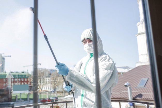 Koronawirus pandemia. Dezynfektor w kombinezonie ochronnym i masce rozpyla środki dezynfekujące w domu lub biurze. Ochrona przed chorobą COVID-19. Zapobieganie rozprzestrzenianiu się wirusa zapalenia płuc na powierzchniach.