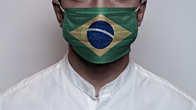 Koronawirus pandemia. Koncepcja kwarantanny wirusa Corona, Covid-19. Męska twarz pokryta jest ochronną maską medyczną, pomalowaną na kolory flagi Brazylii