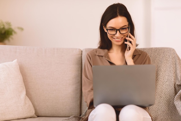 Korporacyjna komunikacja uśmiechnięta dziewczyna rozmawiająca przez telefon komórkowy pracująca na laptopie w domu siedząca na