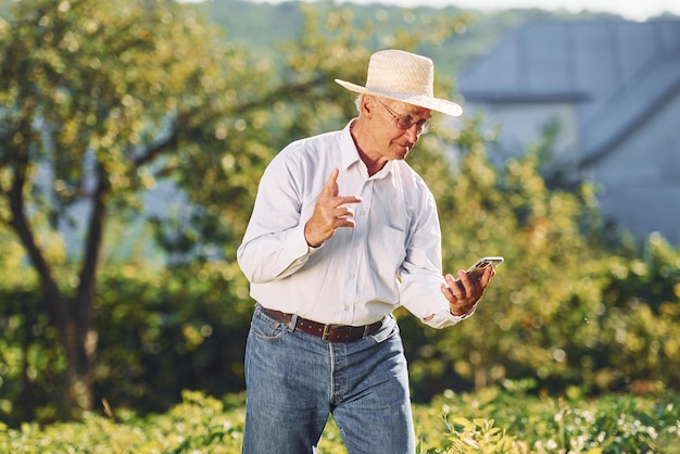 Korzystanie ze smartfona Starszy mężczyzna stoi w ogrodzie w ciągu dnia