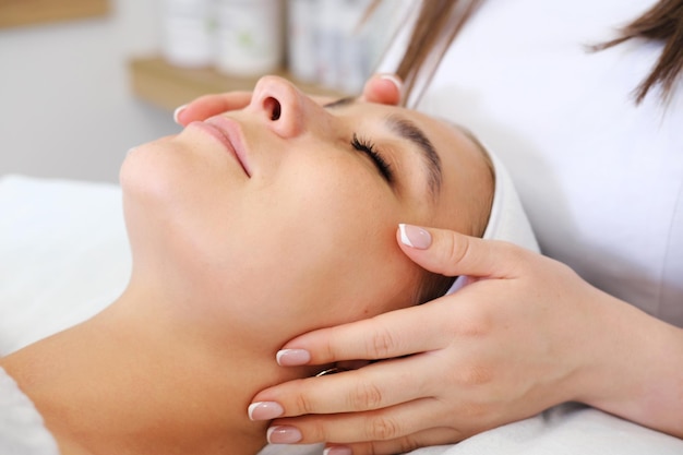 Kosmetolog kładzie ręce na twarzy wykonując zabiegi kosmetyczne Spokojny model leżący na fotelu kosmetycznym z zamkniętymi oczami czekający na masaż twarzy Koncepcja pielęgnacji skóry