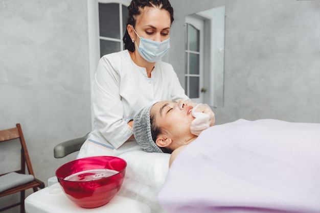 Kosmetolog oczyszcza skórę klientki salonu piękności przed zabiegiem i masażem twarzy Pojęcie piękna i zdrowia kosmetologia skóra pokryta pryszczami