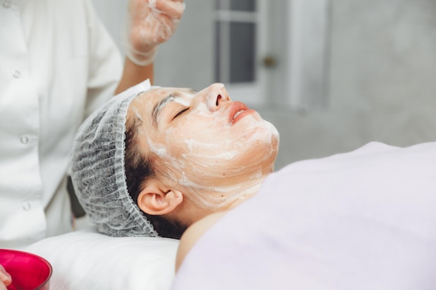 Kosmetolog oczyszcza skórę pianką Zabieg pielęgnacyjny dla kobiecej skóry Kosmetyki naturalne Piękna twarz Zabieg kosmetyczny twarzy Terapeutyczny krem peelingujący
