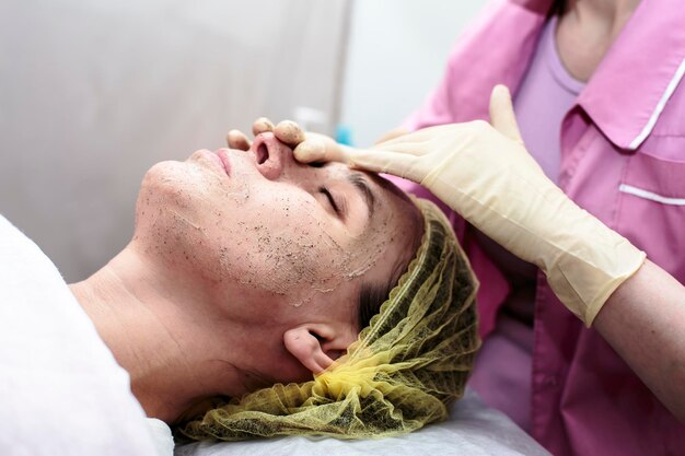 Kosmetolog oczyszcza skórę twarzy pacjentki za pomocą peelingu w gabinecie.