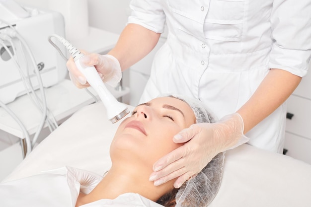 Kosmetolog sprawia, że ultradźwięki napinają skórę w celu odmłodzenia twarzy kobiety za pomocą fonoforezy