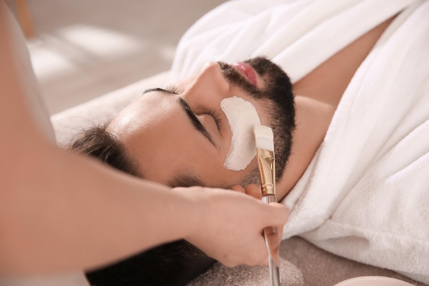 Kosmetolog stosujący maskę na twarzy mężczyzny w salonie spa