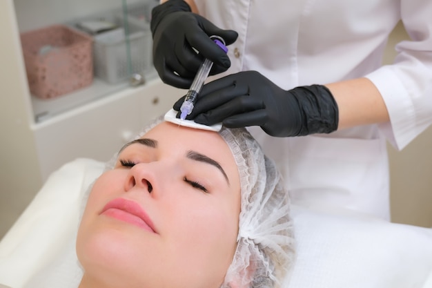 Kosmetolog wstrzykuje strzykawkę w skórę młodej kobiety.