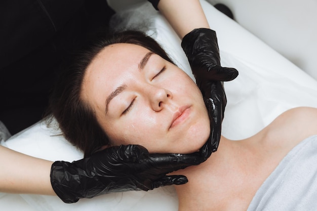 Kosmetolog wykonuje kosmetyczny masaż twarzy dla zrelaksowanej twarzy młodej kobiety w spa Pielęgnacja twarzy masaż koncepcja kosmetologii pielęgnacji skóry
