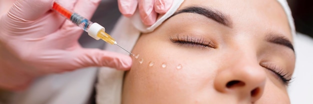 Kosmetolog wykonuje odmładzające zastrzyki przeciwzmarszczkowe na twarz pięknej kobiety Kobieca kosmetologia estetyczna w gabinecie kosmetycznym