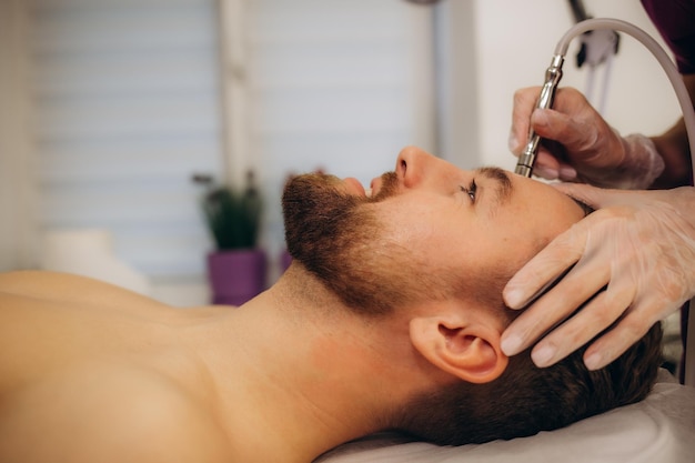 Zdjęcie kosmetolog wykonuje procedurę mikrodermabrasji skóry twarzy w salonie kosmetycznym kosmetologia dla mężczyzn i profesjonalna pielęgnacja skóry zdjęcie wysokiej jakości