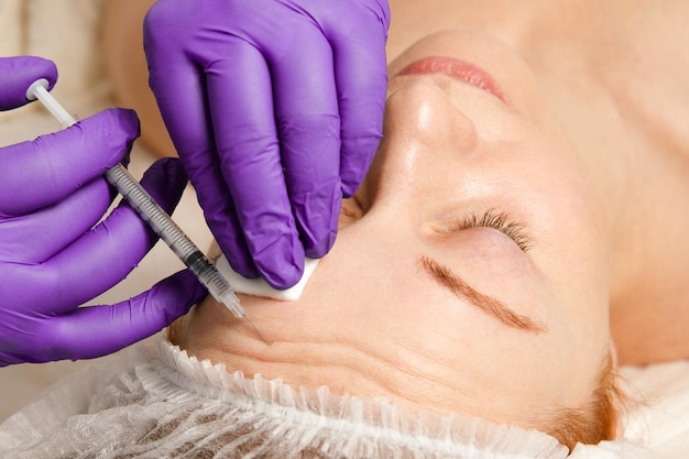 Zdjęcie kosmetolog wykonuje zabieg odmładzających iniekcji na twarz w celu ujędrnienia i wygładzenia zmarszczek na skórze kobiecej twarzy kosmetyczna pielęgnacja skóry w gabinecie kosmetycznym