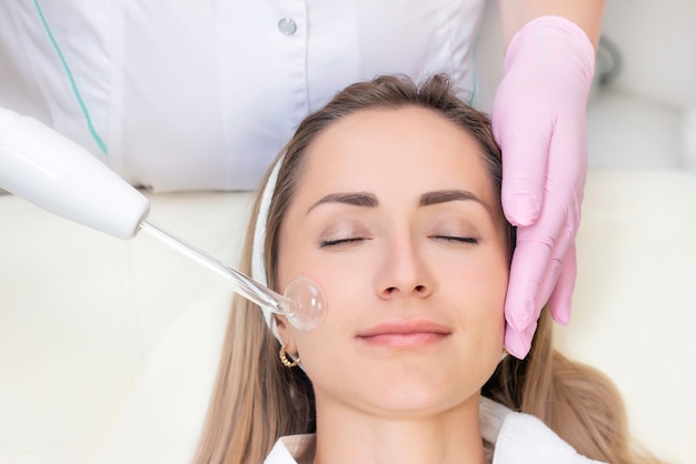 Kosmetolog wykonuje zabieg pulsacyjny na twarzy młodej kobiety.