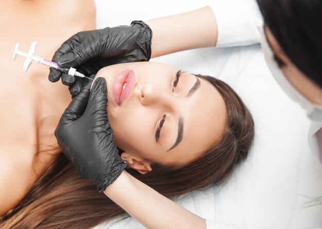 Kosmetolog wykonuje zastrzyki lipolityczne, aby spalić tłuszcz na kobiecym podbródku na podwójnym podbródku Kosmetologia estetyczna kobiet w salonie kosmetycznymKoncepcja kosmetologii