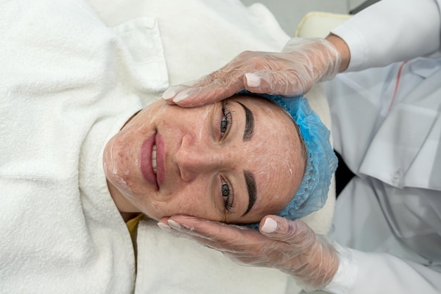 Kosmetyczka lub dermatolog nakłada białą maskę na twarz klienta za pomocą pędzla