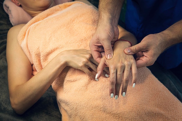 Kosmetyczka masująca dłoń klienta salonu spa Profesjonalny masażysta ugniata dłoń młodej kobiety