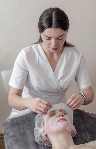 Kosmetyczka nakłada maskę kolagenową na twarz kobiety Kosmetolog pracuje z kobietą w salonie spa