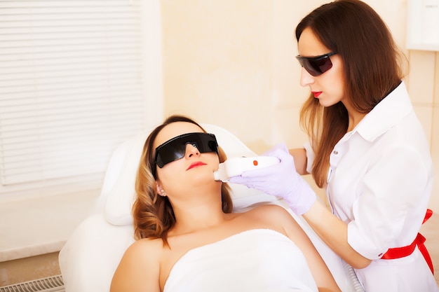 Kosmetyczka poddaje zabieg depilacji laserowej twarzy młodej kobiety w klinice urody.