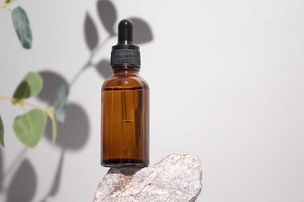 Kosmetyczna butelka serum olej na kamiennym stojaku z gałęzi eukaliptusa na szarym tle Koncepcja naturalnych kosmetyków Produkt do pielęgnacji skóry Koncepcja piękna do pielęgnacji twarzy