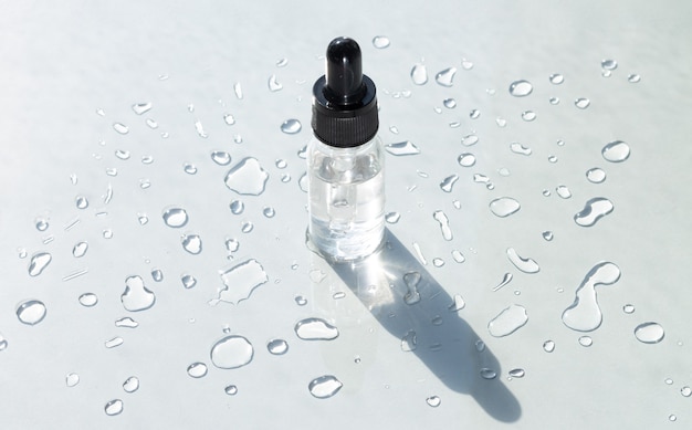Kosmetyczne serum do pielęgnacji skóry w przezroczystej szklanej butelce na szarej powierzchni z kroplami wody