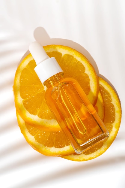 Zdjęcie kosmetyczny organiczny ekstrakt witaminy c kawałki pomarańczy i butelka z serumem na białym tle z widokiem z góry w cieniu palmy