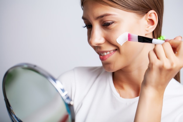 Zdjęcie kosmetyki do twarzy kobiety, kobieta przed lustrem nakłada krem do pielęgnacji skóry