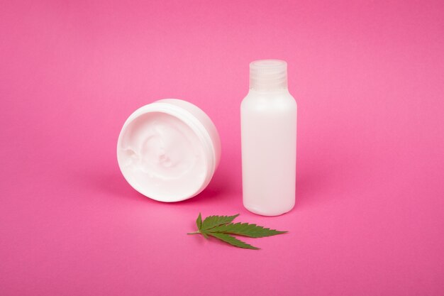 Kosmetyki pielęgnacyjne do ciała, przeciwstarzeniowe do pielęgnacji skóry z ekstraktem z marihuany na różowym tle.